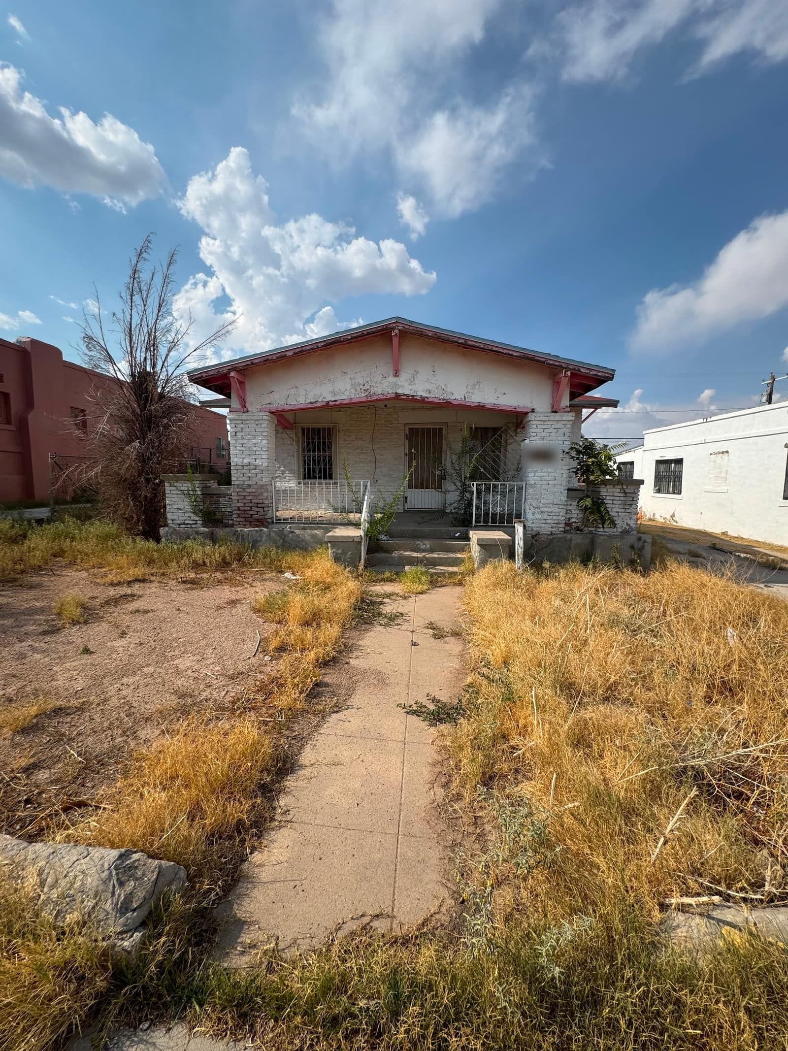 Early-1900s brick bungalow in central El Paso with a covered front porch and an overgrown yard