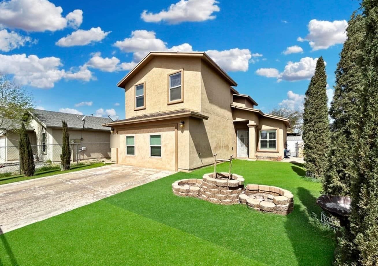 Two-storey stucco house in northeast El Paso with a turf front yard, fire pit and cypress trees