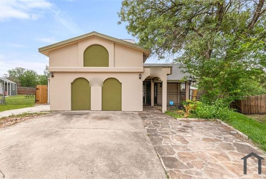 Two-storey stucco house in San Antonio with arched green garage doors and a flagstone path